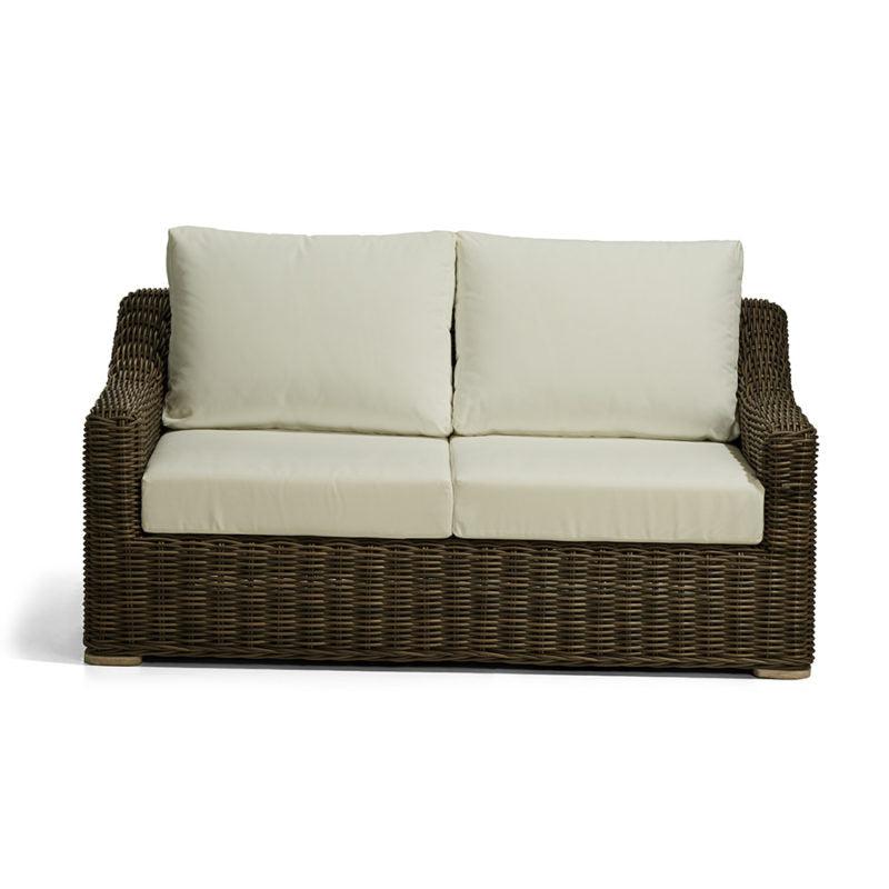Sofá de dos plazas con estructura de mimbre marrón oscuro y cojines de asiento y respaldo en color crema claro. No hay inscripciones visibles ni detalles escritos en el producto.