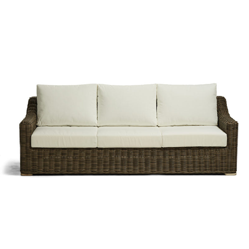 Sofá de tres plazas con base de mimbre marrón oscuro y cojines gruesos de color crema claro en el asiento y respaldo. No hay ninguna inscripción visible en el producto.