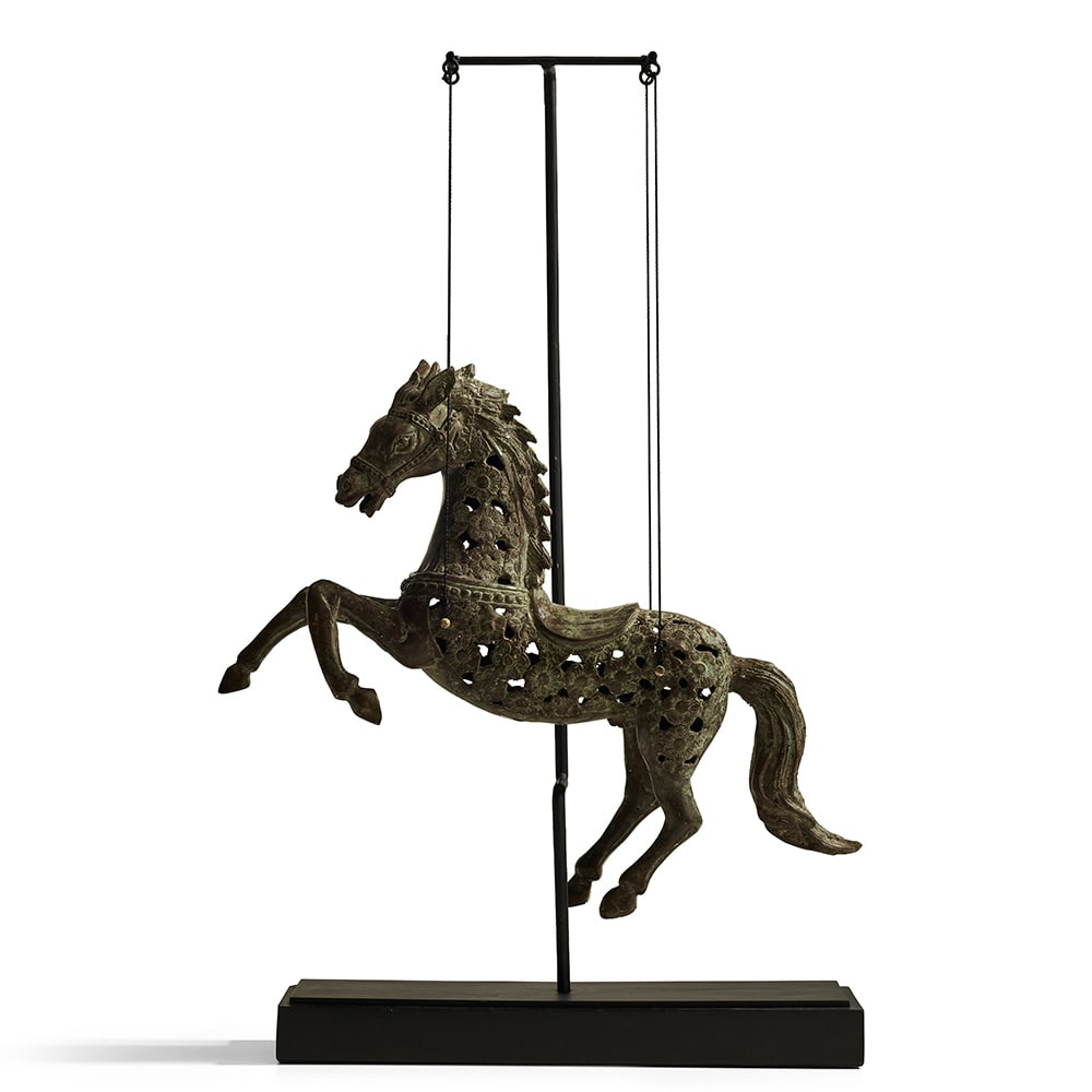 Figura decorativa de un caballo con diseño calado y acabado de bronce envejecido, montado sobre una base negra con soporte metálico vertical.