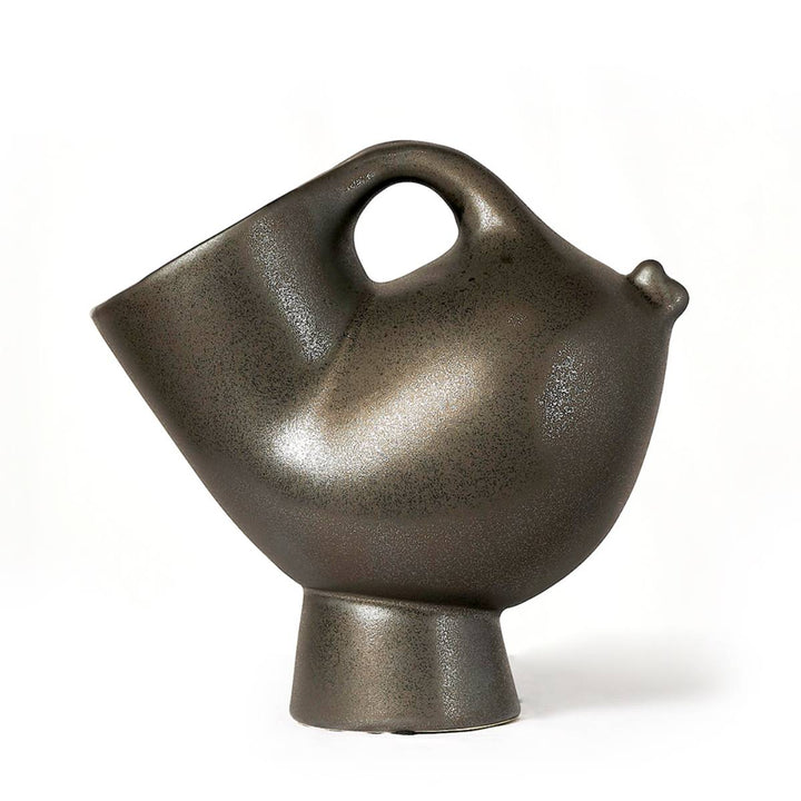 Jarra de cerámica con forma escultórica moderna, con acabado metálico oscuro y una silueta que recuerda a un ave estilizada, con un asa circular en la parte superior y una boquilla sutil.