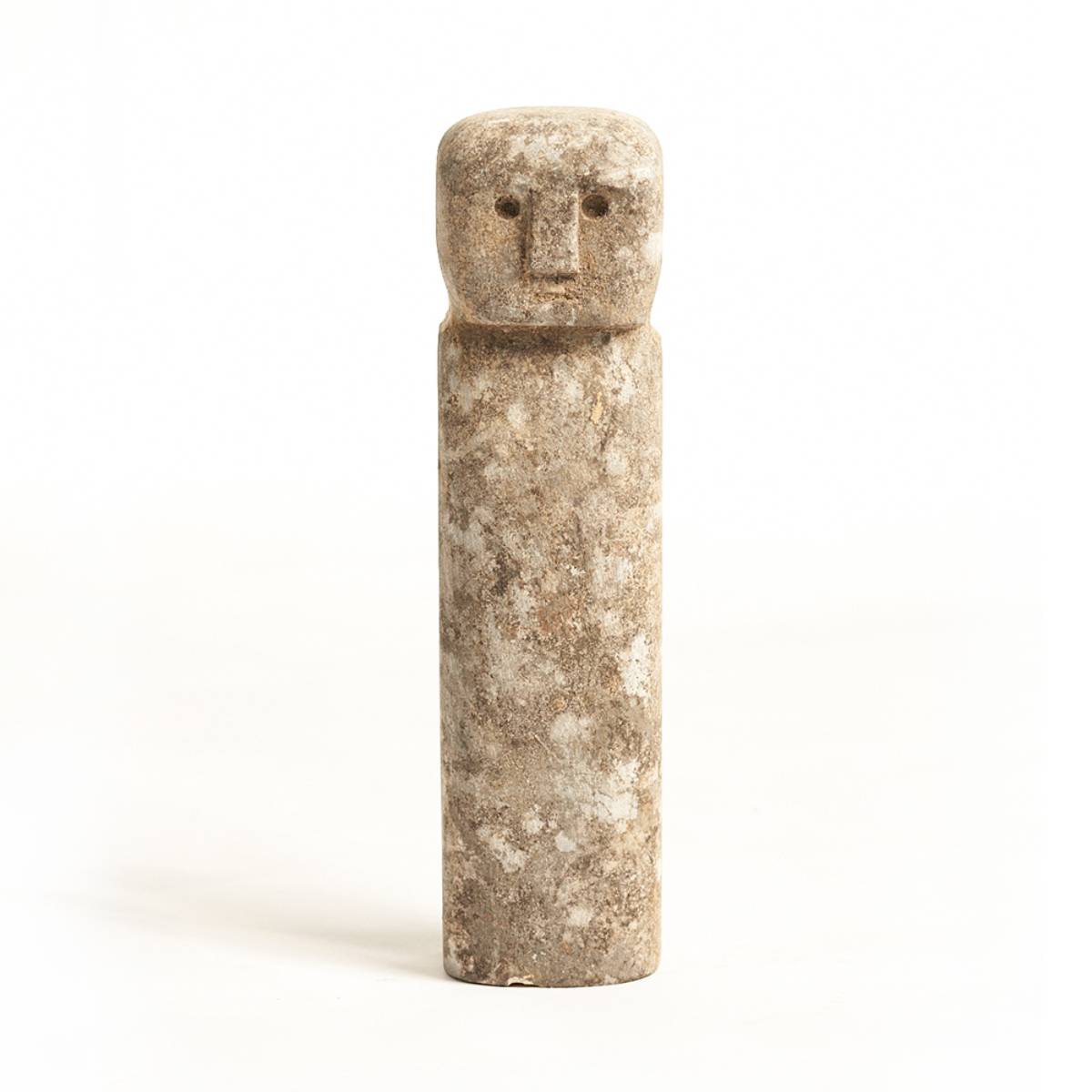 Figura escultórica de piedra con cuerpo cilíndrico y cabeza rectangular. Presenta un rostro esquemático con ojos y nariz tallados en bajo relieve.