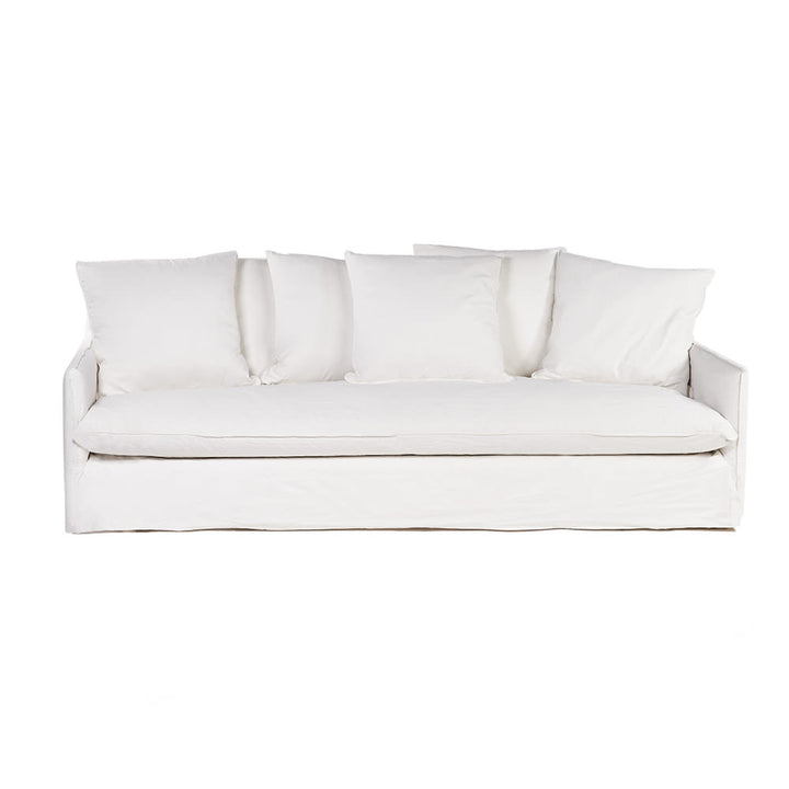 Sofá de tres plazas completamente tapizado en tela blanca, con cinco cojines sueltos en el respaldo y un asiento largo y mullido. El diseño es minimalista y contemporáneo.