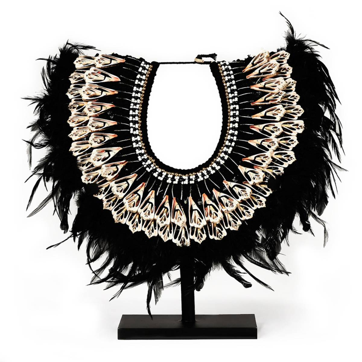 Collar decorativo en forma de media luna con múltiples plumas negras y detalles ornamentales en tonos claros y rosados, dispuesto en un soporte de exhibición. Los elementos decorativos incluyen patrones simétricos y tiras de cuentas en blanco y negro.