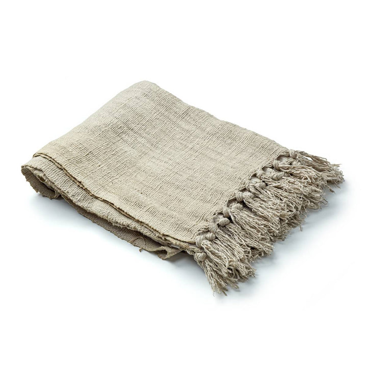 Manta tejida de color beige con textura rústica y flecos en uno de los bordes, doblada cuidadosamente.