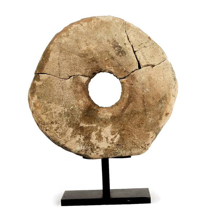 Rueda de piedra circular con un agujero central, presenta grietas visibles y está montada sobre un soporte negro de exhibición.