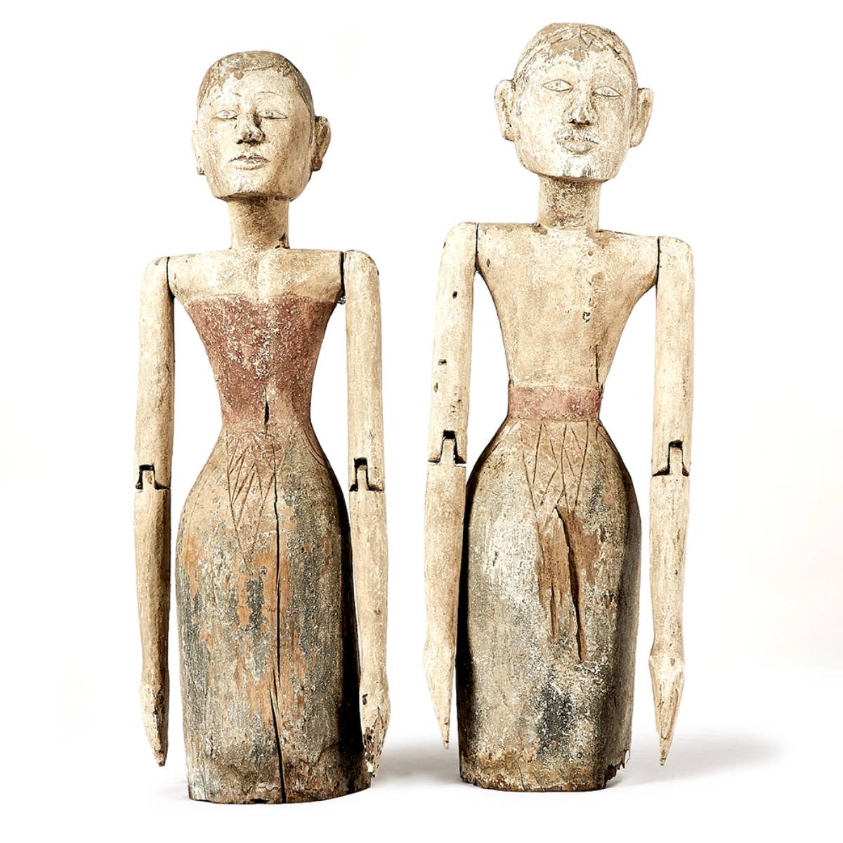 Dos figuras talladas en madera con forma humana, de aspecto estilizado y acabados rústicos, pintadas en tonos tierra. Ambas tienen brazos articulados y detalles grabados en la parte inferior del torso que sugieren vestimenta.