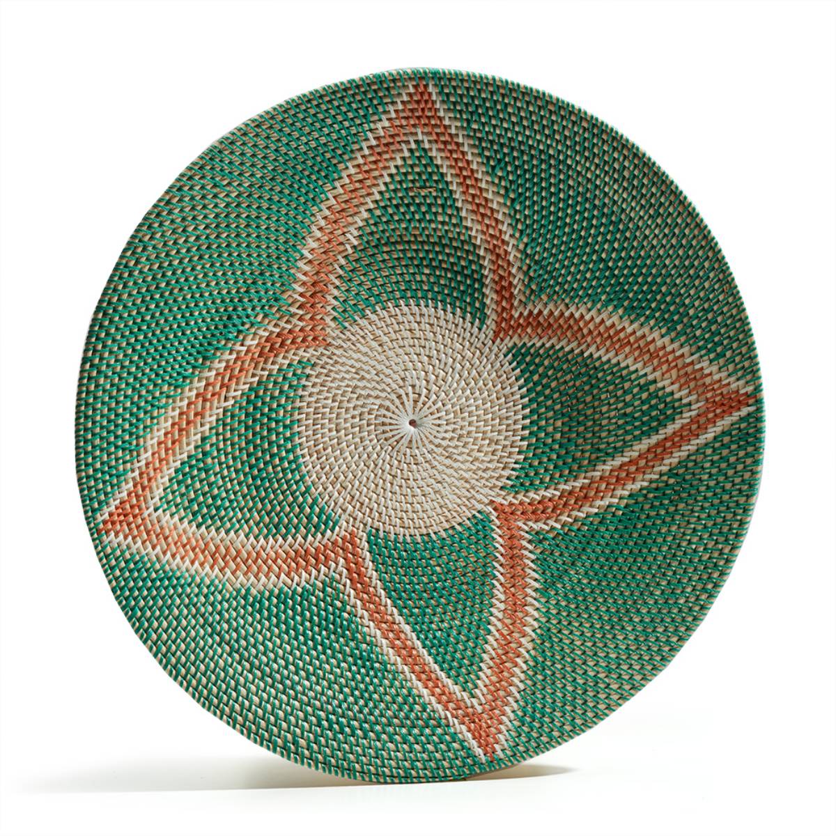 Plato decorativo tejido a mano con fibras naturales, presenta un patrón simétrico en forma de flor con colores beige, verde y terracota.