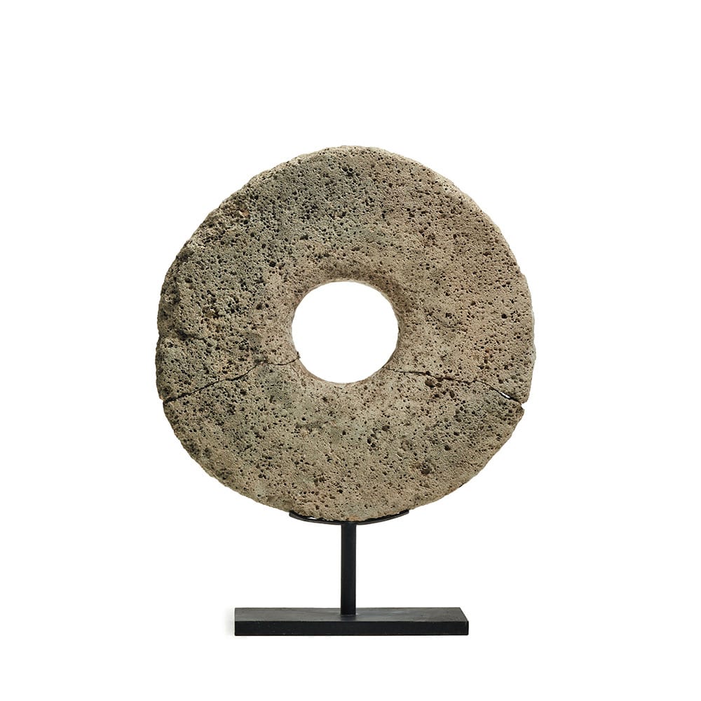 Objeto decorativo en forma de disco de piedra volcánica con un agujero central, montado sobre una base metálica negra para exhibición.