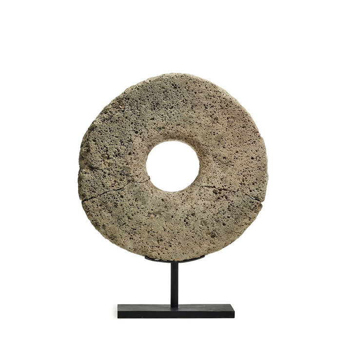 Objeto decorativo en forma de disco de piedra volcánica con un agujero central, montado sobre una base metálica negra para exhibición.