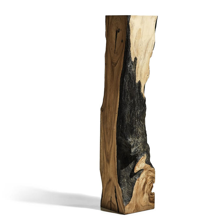 Bloque vertical de madera tallada con una textura orgánica que mezcla tonos naturales de madera con una gran zona ennegrecida que parece carbonizada o quemada.
