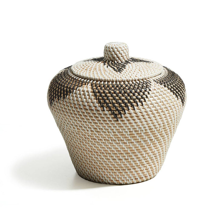 Recipiente tejido con tapa, de forma redondeada y patrón geométrico con colores crema, beige y marrón oscuro. No presenta detalles escritos visibles.