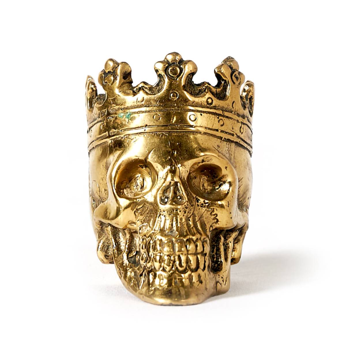 Una figura decorativa con forma de calavera dorada con una corona también dorada sobre la cabeza. El acabado metálico brillante y los detalles de la corona le dan un aspecto lujoso y llamativo.