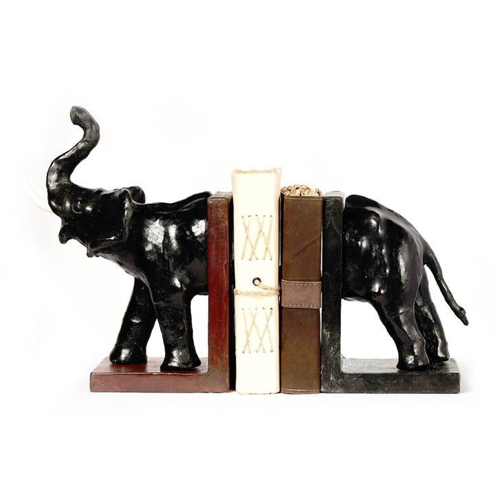 Sujetalibros decorativo compuesto por dos piezas de resina negra con forma de elefante dividido, una sosteniendo la parte delantera y otra la trasera. Entre ambas piezas hay tres libros, dos con tapas marrones y uno blanco con costuras en forma de "XX".