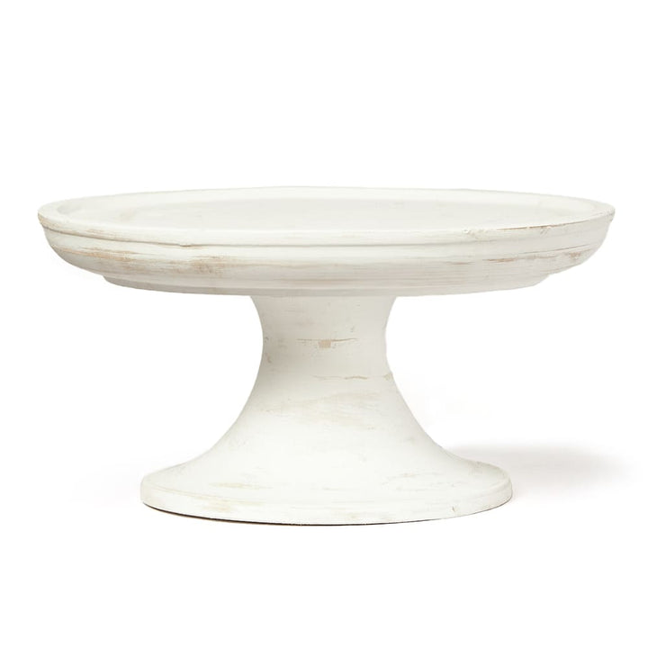 Base de torta de cerámica o madera pintada de blanco con acabado envejecido, de forma circular y con pedestal ancho. No se observan inscripciones ni marcas visibles en el producto.