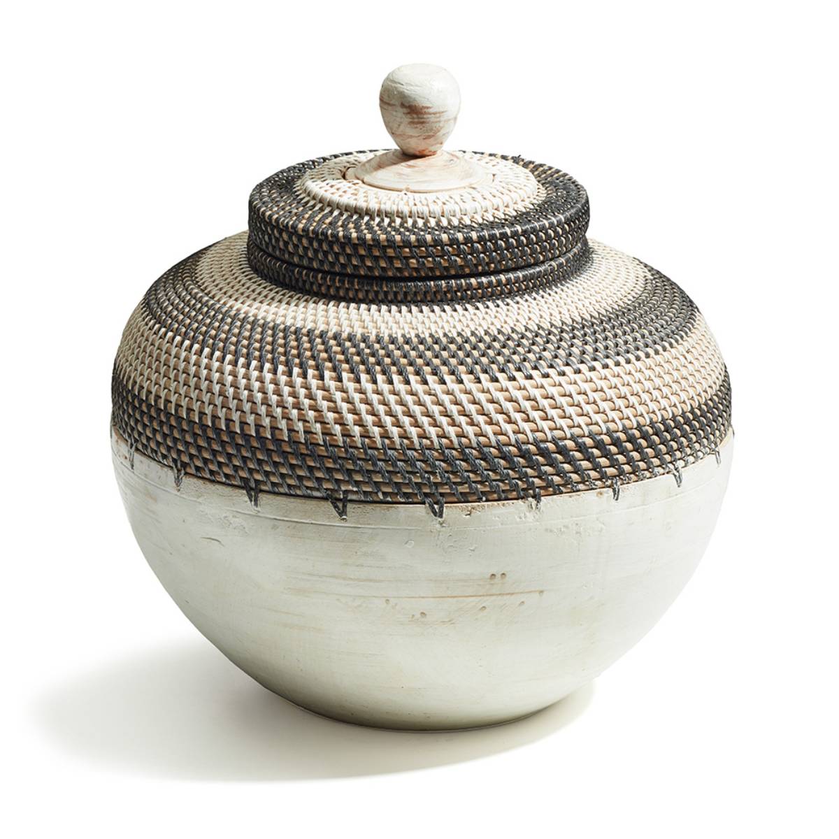 Recipiente con tapa en forma de esfera, hecho de cerámica clara con una parte superior decorativa con patrón tejido de fibras oscuras y claras. Tiene un diseño artesanal que combina texturas naturales y contrastes definidos.