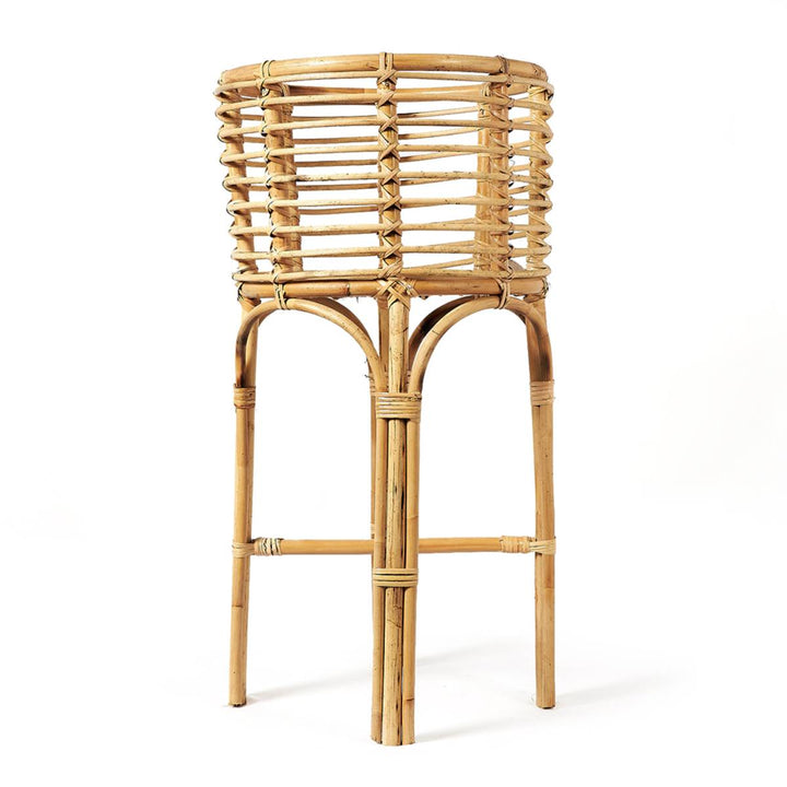 Soporte alto de mimbre tejido con estructura firme, utilizado comúnmente como porta macetas o elemento decorativo. Presenta un diseño natural con un patrón circular entrelazado en la parte superior.